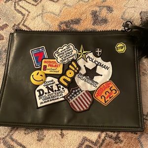Large black clutch bag with patches and a fluffy pom on the zipper